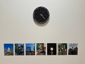 Two artworks hang mounted on a white museum wall. The top artwork, 'Have you ever fallen in love with a clock?', shows a black clock divided into seven wedges, each labeled with a day of the week in white letters. Seven rectangular images underneath show everyday public sites, like a clock tower and town square, with day-by-day clocks superimposed on the images in place of 60-second clocks.